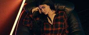 woman wearing black and red checkered dress shirt lying on black leather sofa chair inside well-lit room