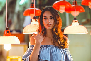 woman wearing blue off-shoulder tops standing near red and white pendant lamps