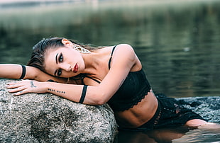 woman in black outfit laying on rock near body of water