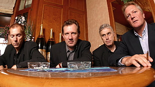 three men in black tops sitting in front of table with four rocks glasses