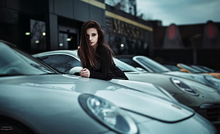 woman in black dress stands beside gray cars
