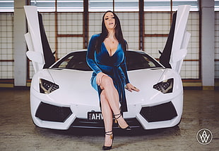 woman in blue plunging neckline dress sitting on white Lamborghini supercar