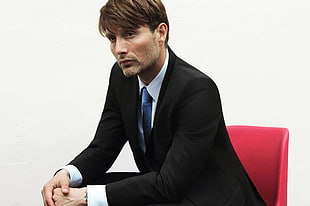 brown haired man in formal suit jacket sitting on red chair