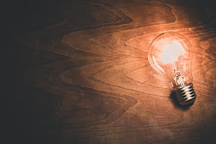 close up image of lighted light bulb on brown wooden surface