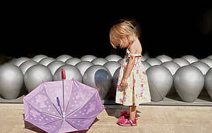 girl in beige and pink floral off-shoulder dress facing purple print opened umbrella