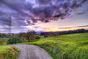empty road in between grass field under gray clouds during sunset
