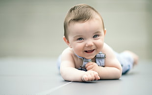 baby in gray overalls crawling while smiling