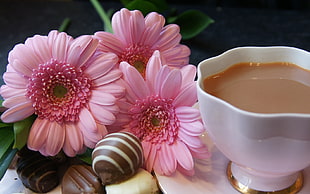 cup of coffee beside pink Gerbera flowers and chocolates