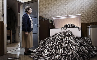 woman wearing white shirt, black cardigan and brown skirt looking at white chest freezer with fishes