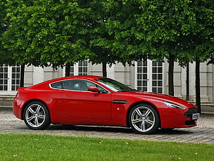 red Aston Martin coupe on gray concrete near green grass field during daytime