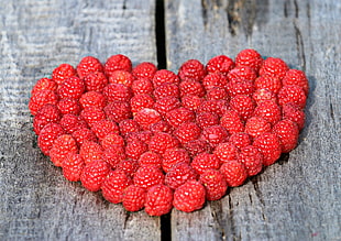 bunch of raspberry in heart shape on brown surface