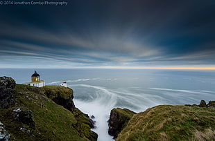 timelapse photography of white and black lighthouse near cliff during golden hour
