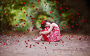 girl wearing red and white floral dress surrounded by red Rose petals