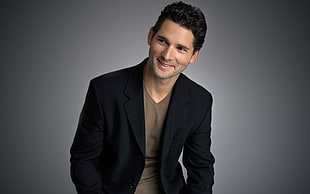 smiling man wearing brown v-neck shirt and black blazer