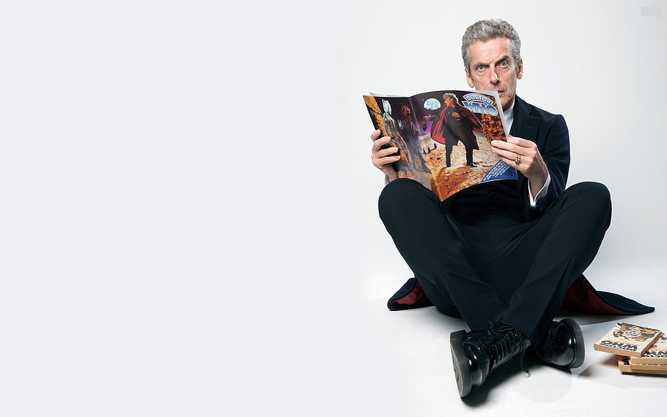 photo of man wearing black suit jacket and dress pants while holding magazine HD wallpaper