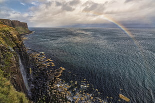 cliff near on ocean under cloudy sky