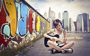 woman playing guitar beside wall with graffiti print