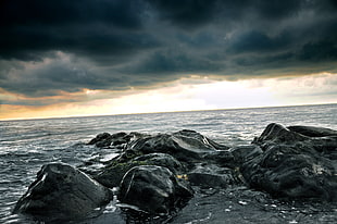 stone formation in body of water under black cloudy sky during daytime