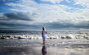 girl in white sleeveless dress in front of ocean waves