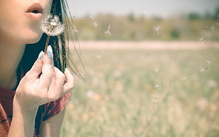 woman wearing red shirt holding and blowing Dandelion flower
