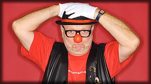 man with clown nose and black framed eyeglasses holds his hat