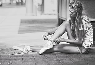 grayscale photo of woman sitting wearing ballet shoes