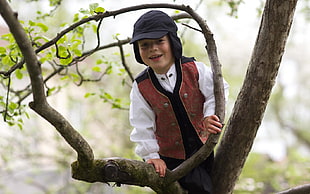 boy on tree wearing red vest