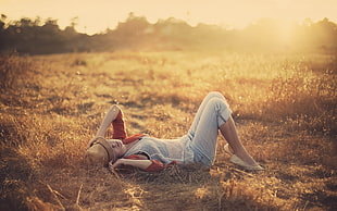woman wearing white tank top and washed gray denim pants laying on brown grass