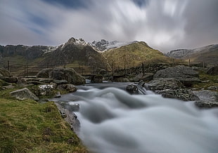 time lapse photograph of river stream between rock formation under gray sky, snowdonia