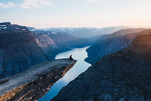 person sitting on the edge, sunset, water, sky, mountains