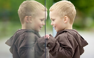 boy in brown jacket facing mirror