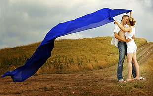 couple kissing on field while holding blue textile