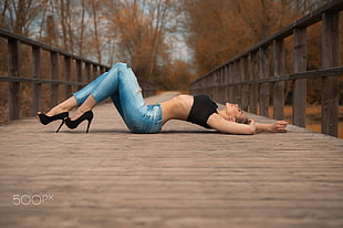 woman wearing distressed acid wash jeans and black crop top lying on footbridge selective focus photography HD wallpaper