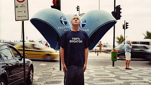 man wearing blue 100% brighton print shirt standing beside black sedan during daytime HD wallpaper