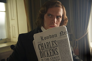 person holding news paper Charles Dickens article close-up photography
