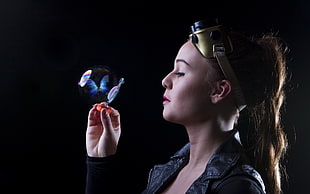 brown haired woman in black jacket holding blue butterfly hologram