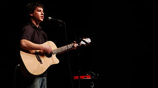 man in black polo shirt playing brown acoustic guitar on stage