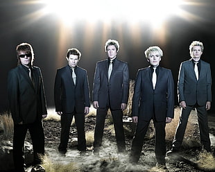 5-man band wearing black suits with lighted background