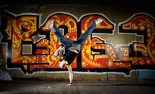 person break dancing near graffiti painted wall