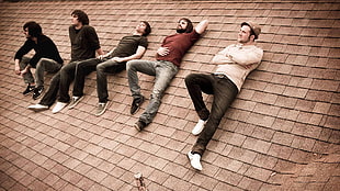 five men sitting and lying on brown roof tiles during daytime