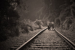 three persons walking on railroad grayscale photo