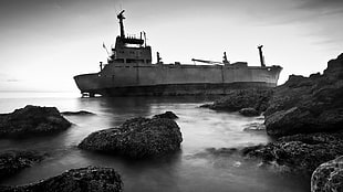 grayscale photo of ship beside rock isles, ship