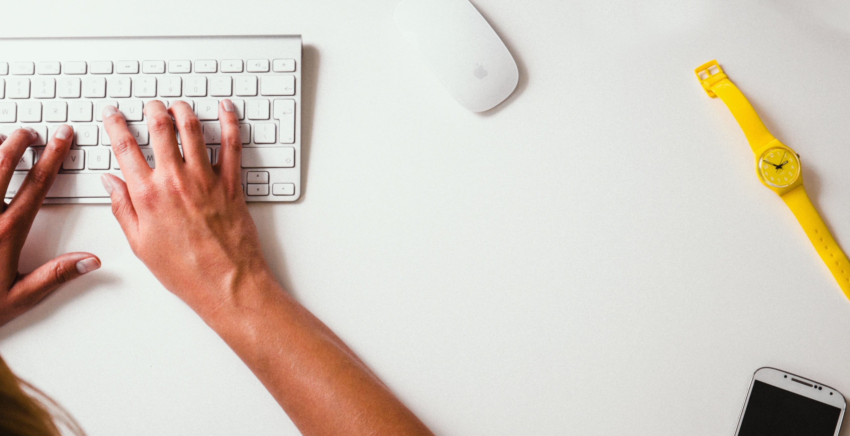 person using Mac Keyboard and Magic Mouse on white table