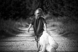 gray scale photo of girl holding a teddy bear while walking