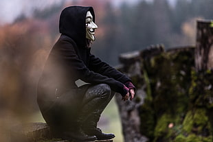 Anonymous man wearing black pullover hoodie with gray denim pants and black leather shoes sitting on brown cut log during daytime HD wallpaper