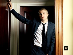 man in black formal suit standing and holding the door frame