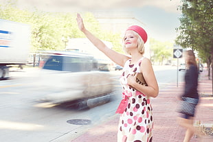 woman wearing white and multicolored dotted sleeveless sheath dress waving for taxi