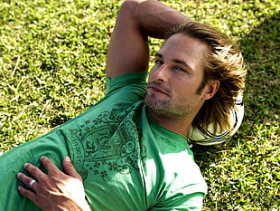 blonde man wearing green crew-neck shirt lying on grass field during daytime