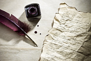 purple feathered quill pen with ink bottle and white paper page