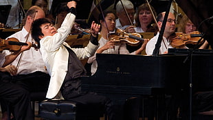 man in white suit jacket playing grand piano with orchestra